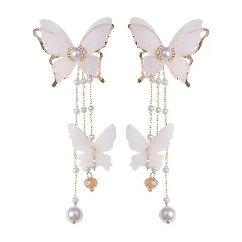 A pair of white butterfly-shaped earrings with tassels, lace details, pearls, and rhinestones.
