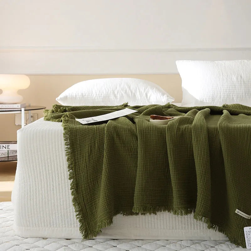 Four-layer cotton gauze blanket with tassel trim shown in avocado green colour.