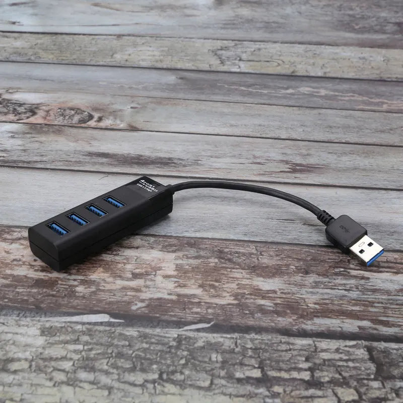 Black USB 3.0 hub with four ports and a 30 cm attached cable on a desk.
