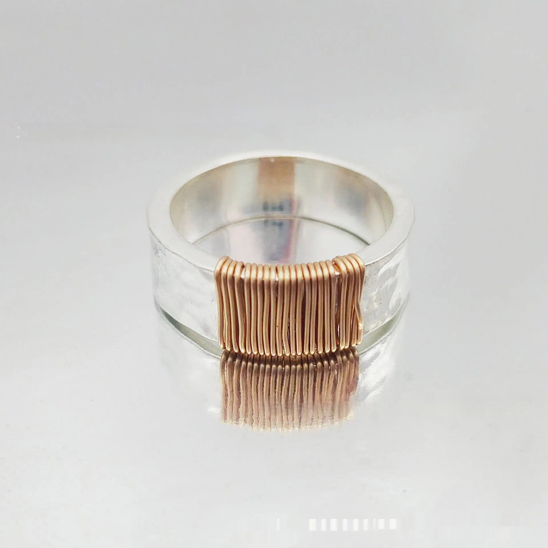 Geometric copper ring bracelet with a wide face and irregular coil design in a silver gold colour.