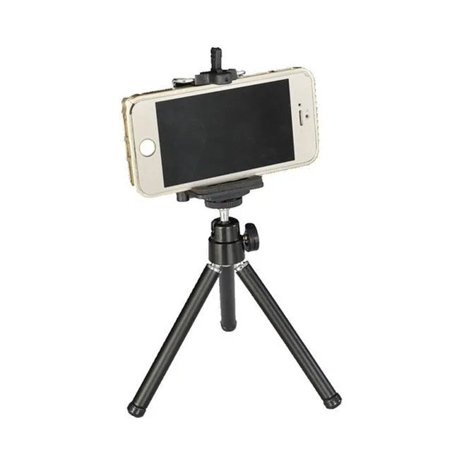 Black mini flexible tripod extended on a table with a silver U-shaped phone clip attached.