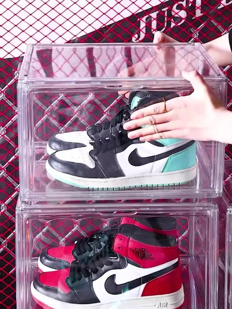 Clear acrylic shoe storage box with magnetic side door open, showing shoes inside.