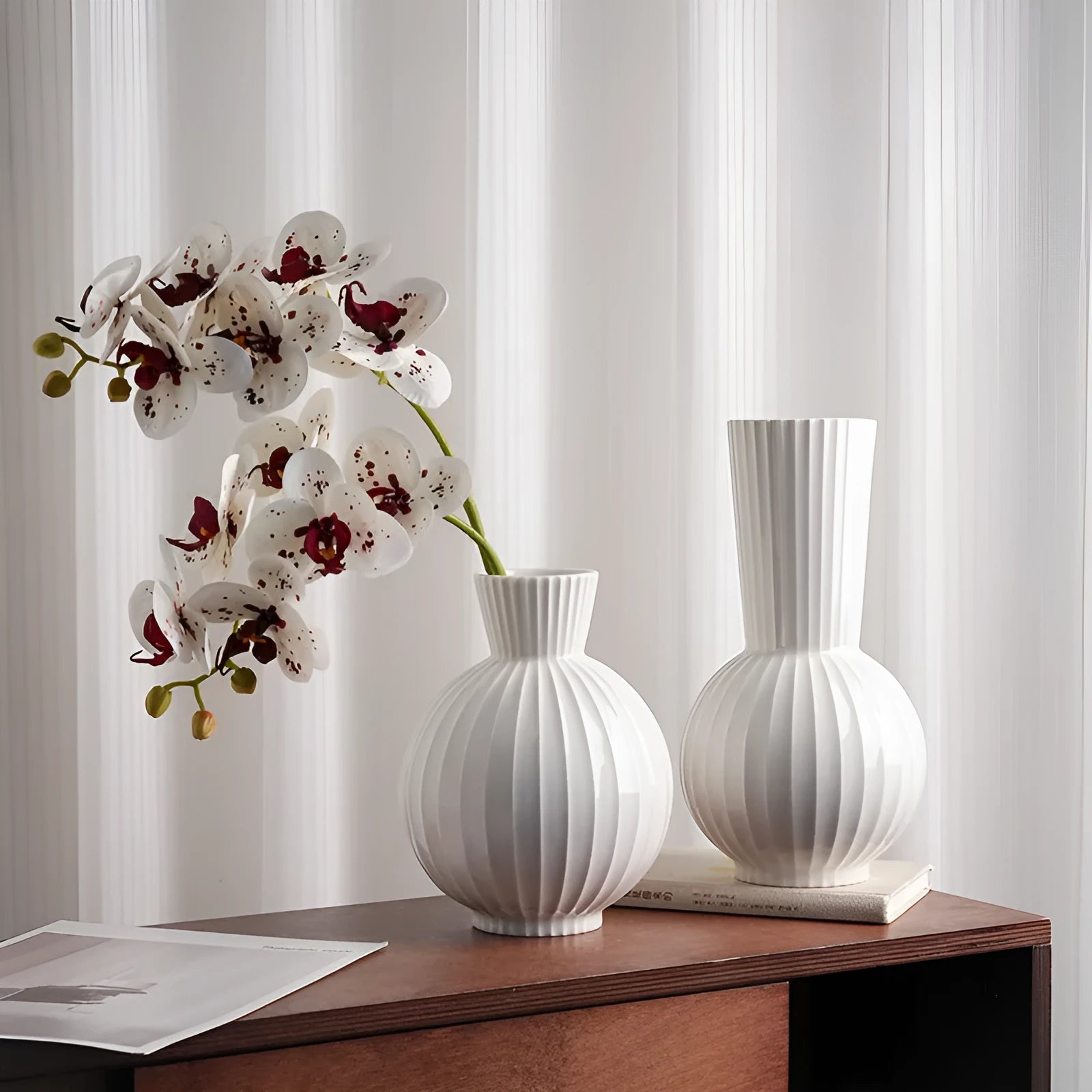 White ceramic ball vase with blue stripes and artificial blue orchid stems on a wooden table.