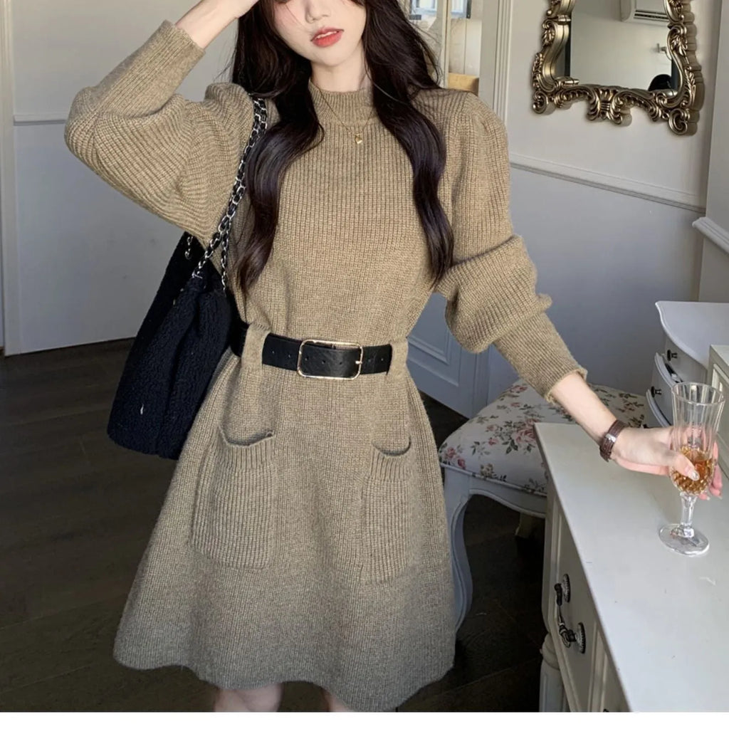 A woman wearing a long sleeve, loose knitted dress in a high-waist style with a black belt.
