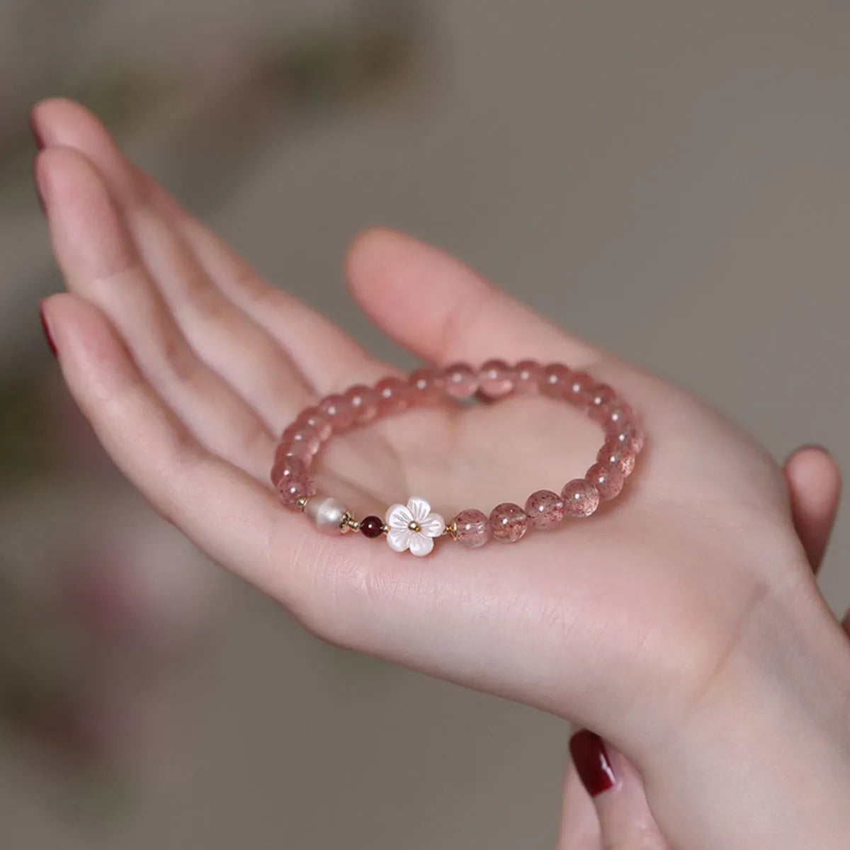 Women's strawberry quartz peach blossom crystal bracelet with floral design on wrist.