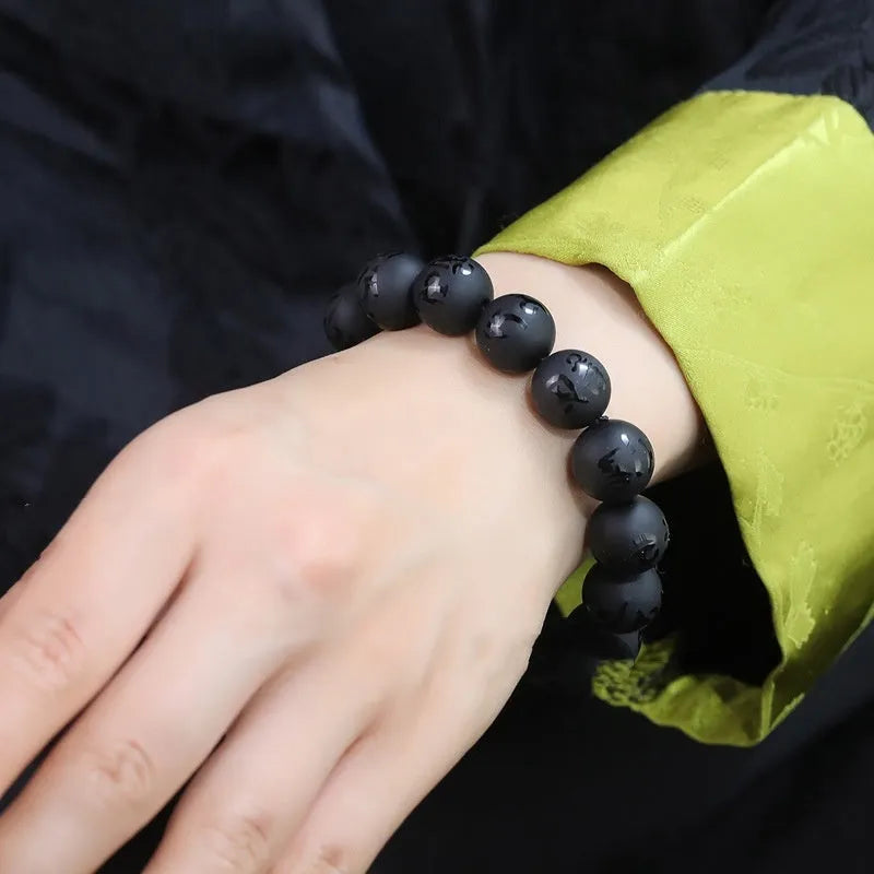 Natural frosted black agate Sanskrit mantra bracelet with Chinese auspicious patterns on a wrist.