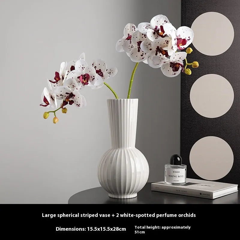 White ceramic ball vase with blue stripes and artificial blue orchid stems on a wooden table.