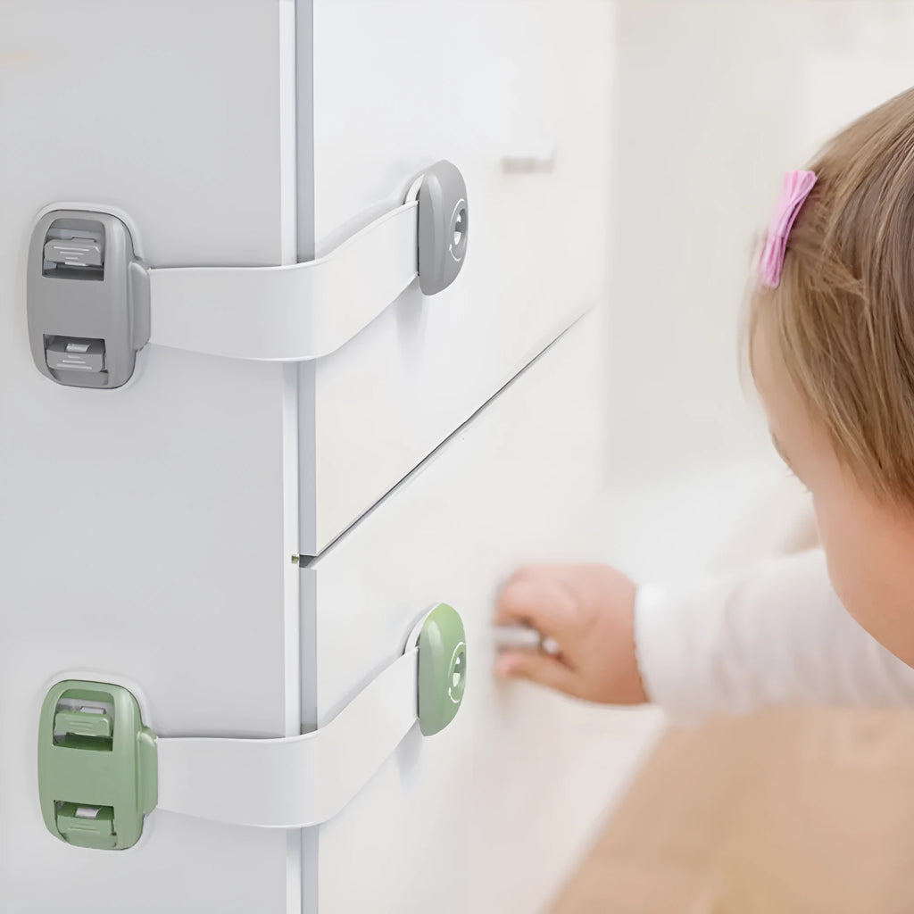 Grey and green adjustable child safety cabinet locks with adhesive backing on a kitchen drawer.