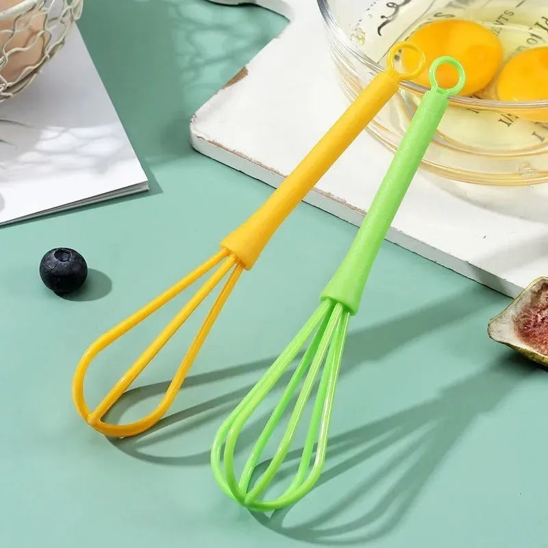 Plastic creative mini manual eggbeater in green and yellow, size 4x18.5 cm, on kitchen counter