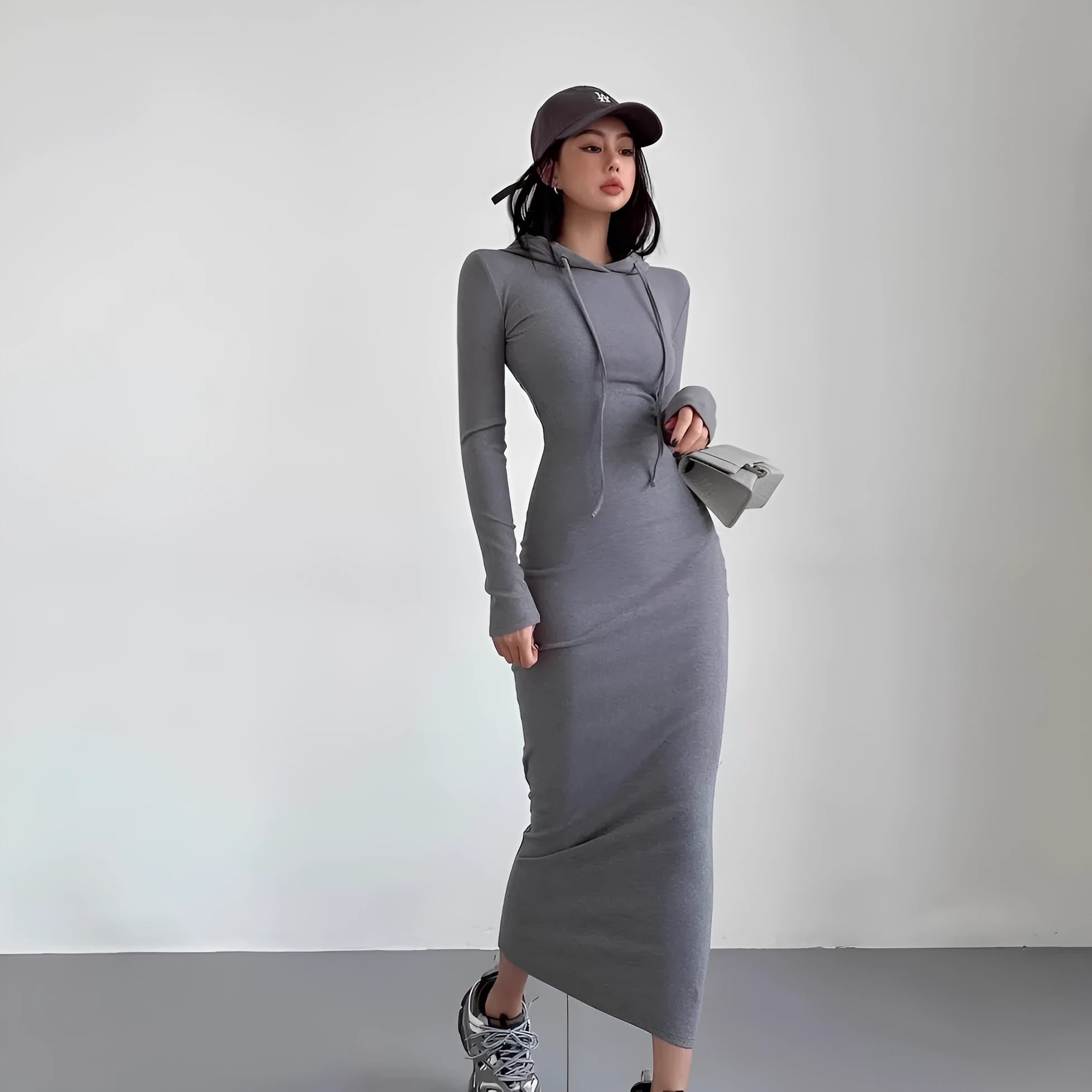 A woman wearing a light grey, long-sleeve polyester sheath dress with an over-the-knee length and high waist.
