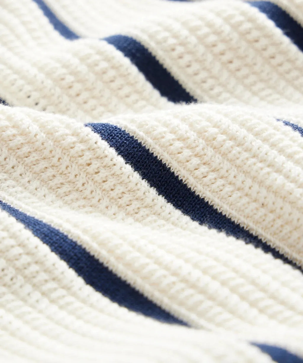 Man wearing a white asymmetric lapel knitted polo shirt with a striped pattern.