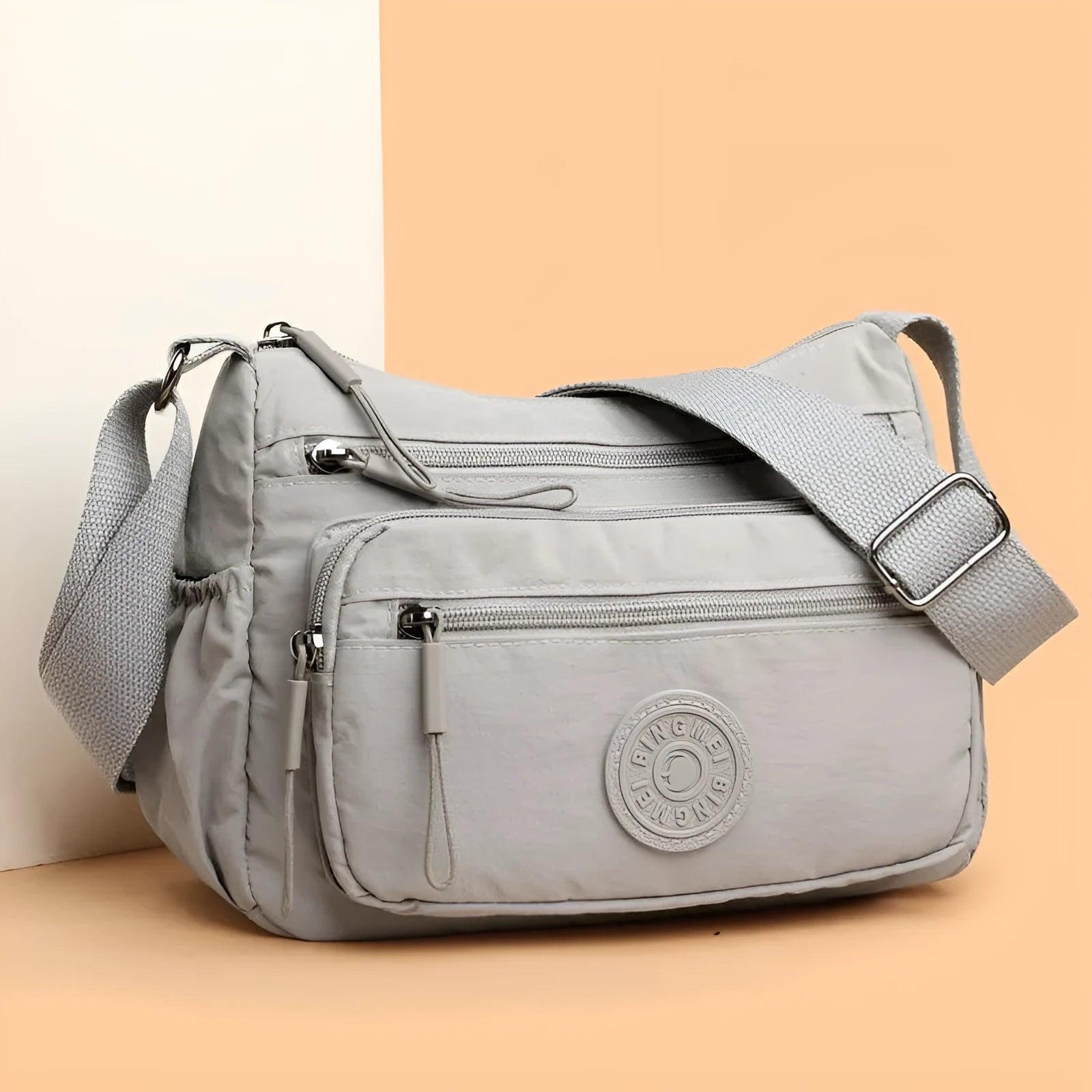 Soft grey nylon crossbody bag with an external pocket and adjustable shoulder strap.