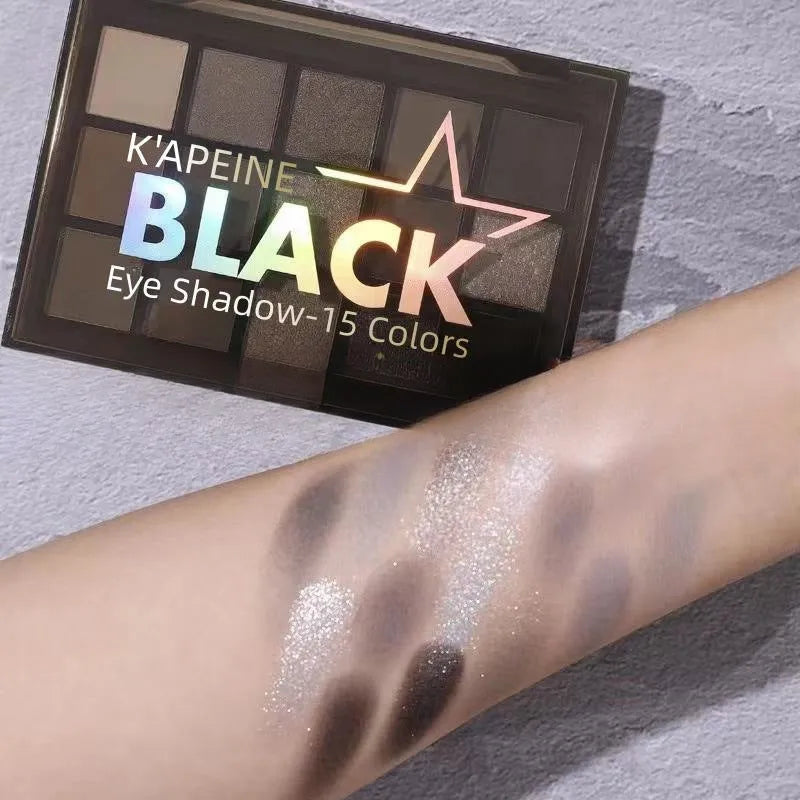 Open 15-pan eyeshadow palette showing matte and shimmer shades in browns, greys, blacks, and blues.