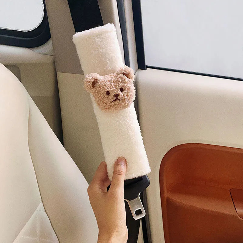 Plush cartoon bear car seat belt shoulder cover in khaki colour, shown next to a car seat.