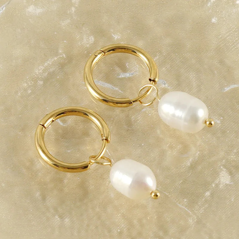 A pair of gold-coloured geometric stud earrings with a central white pearl on a white background.