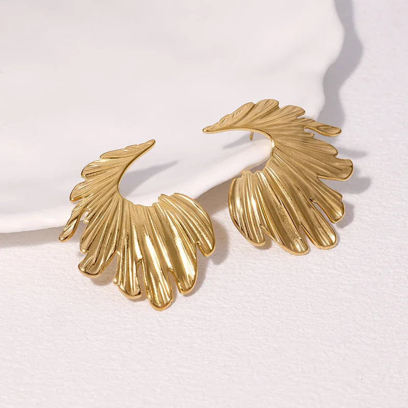 Close-up of a pair of stainless steel leaf-shaped stud earrings on a gold or steel-coloured background.