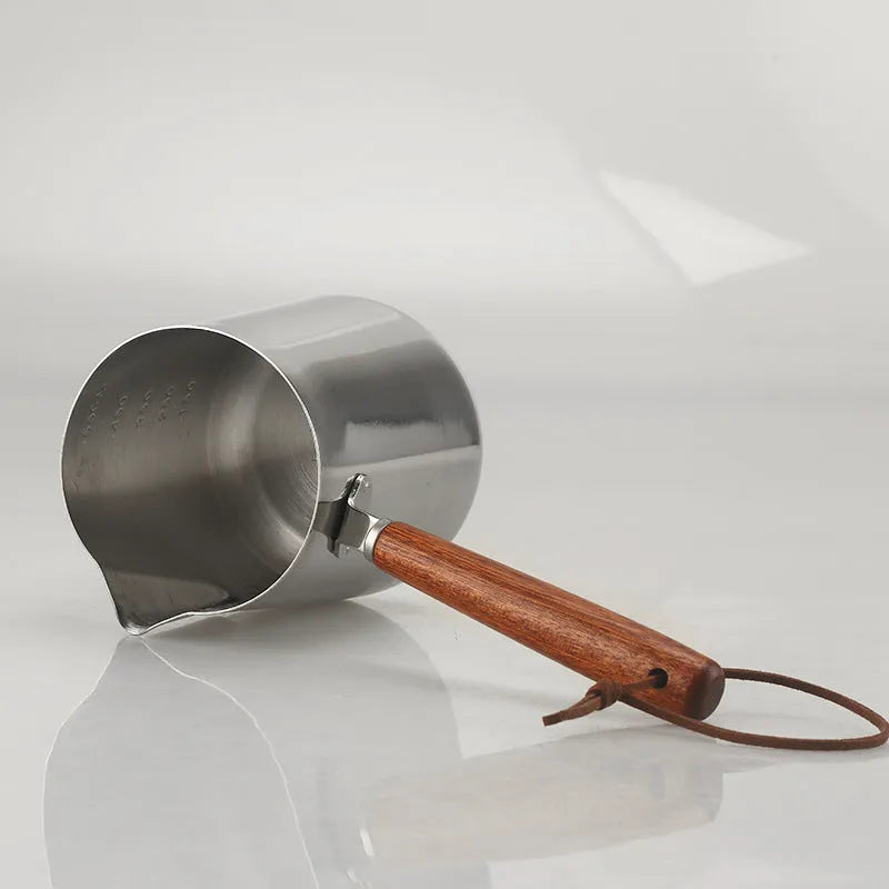 Stainless steel measuring milk cup with wooden handle showing scale markings.
