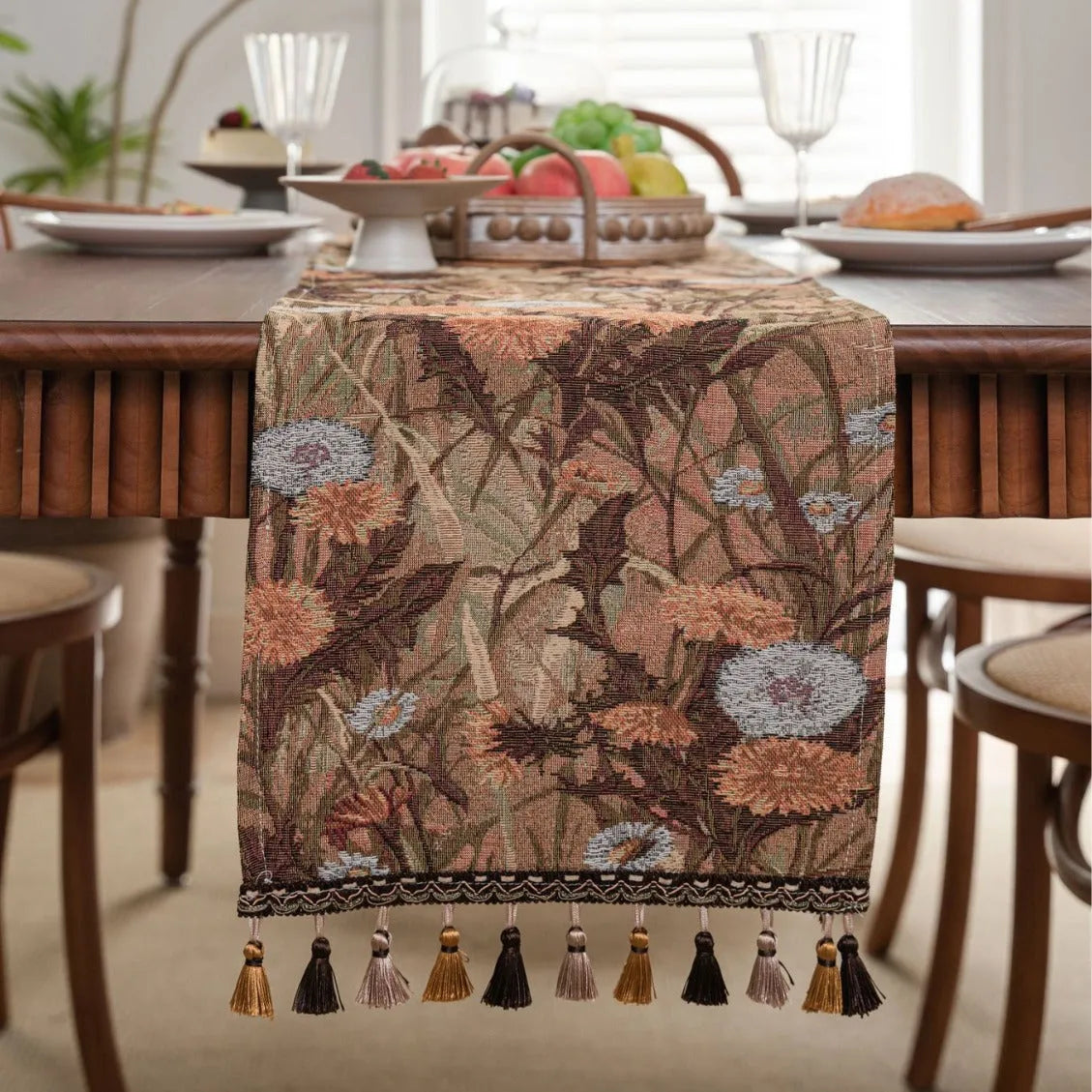 Beige jacquard table runner with floral leaf pattern and long tassels on a dining table.
