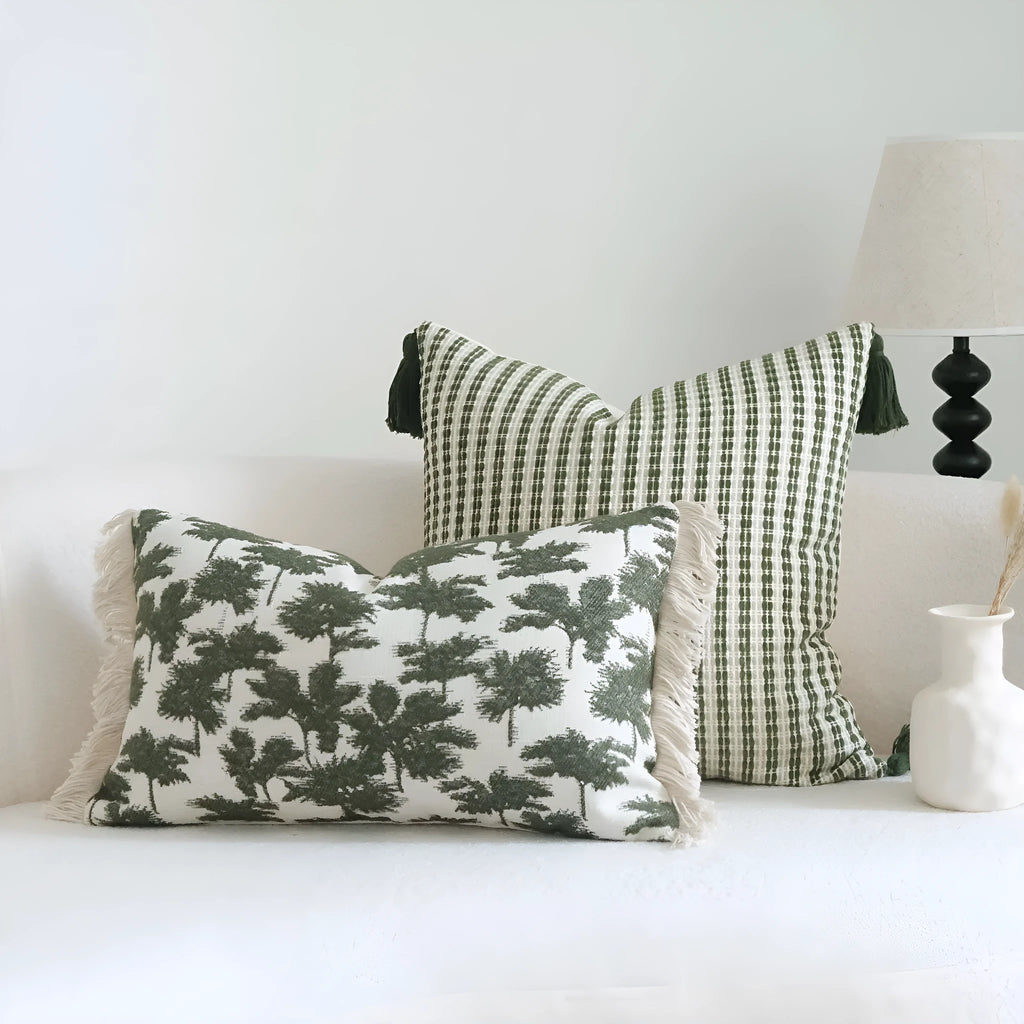Green striped and leaf patterned hotel pillow with tassel trim on a bed.