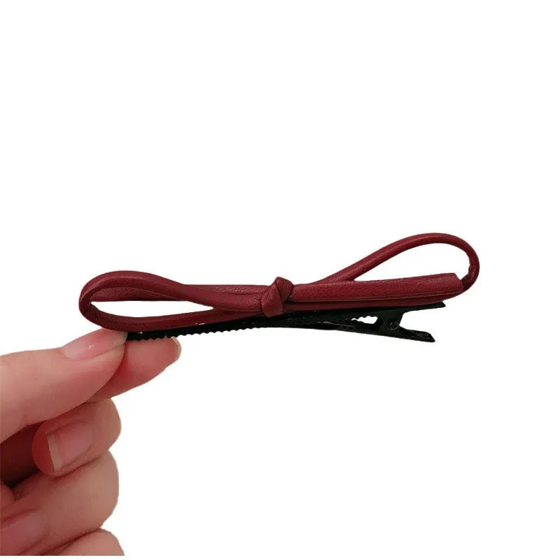 Wine red leather bow barrette hair clip shown on a model or background.
