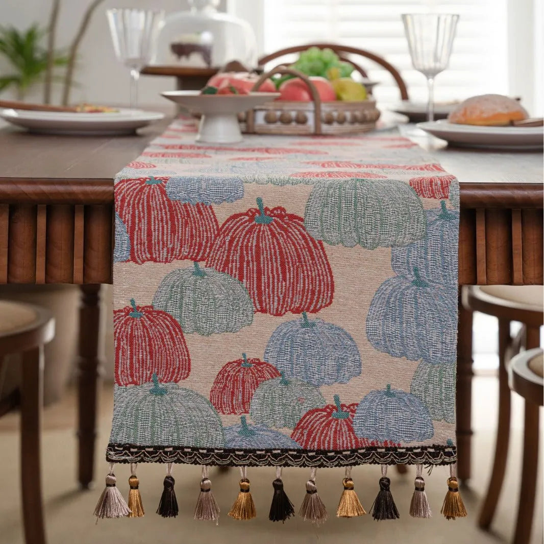 Beige jacquard table runner with floral leaf pattern and long tassels on a dining table.