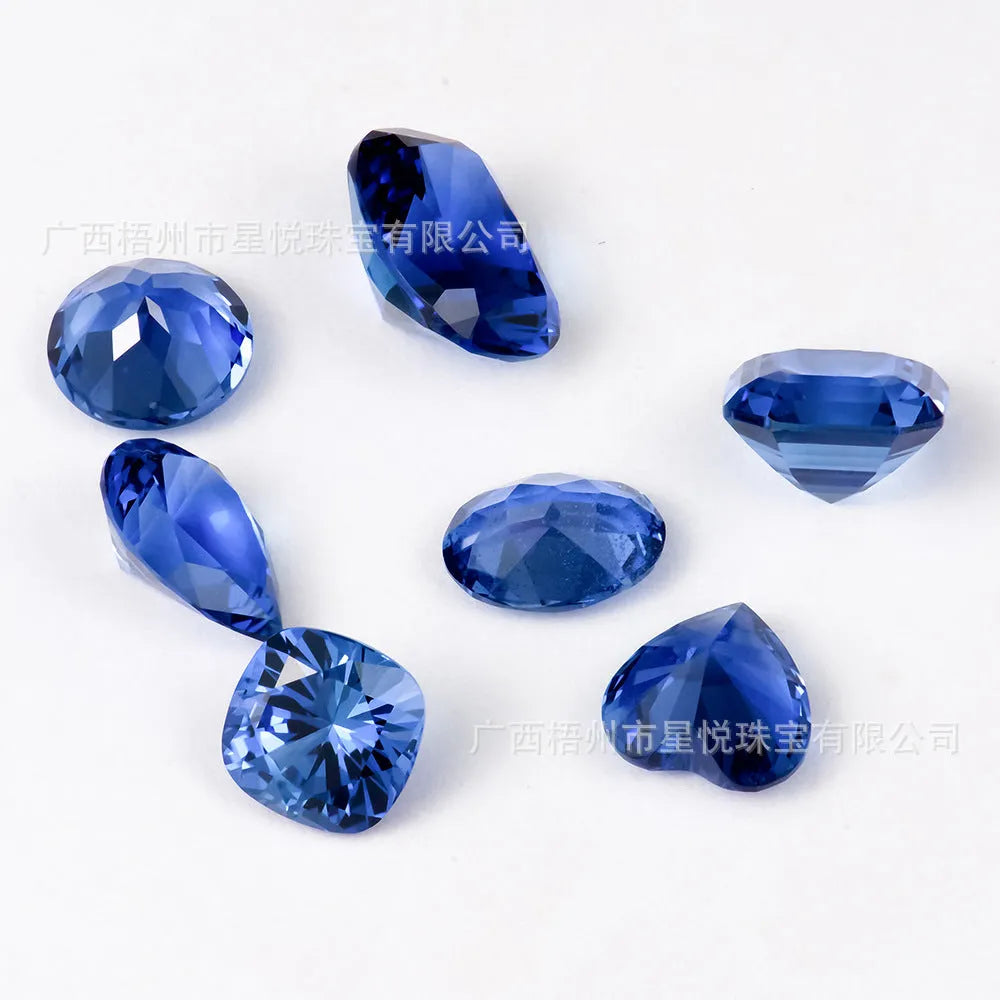A selection of loose royal blue cultivated gemstones in heart, round, and pear shapes on a jeweller's cloth.
