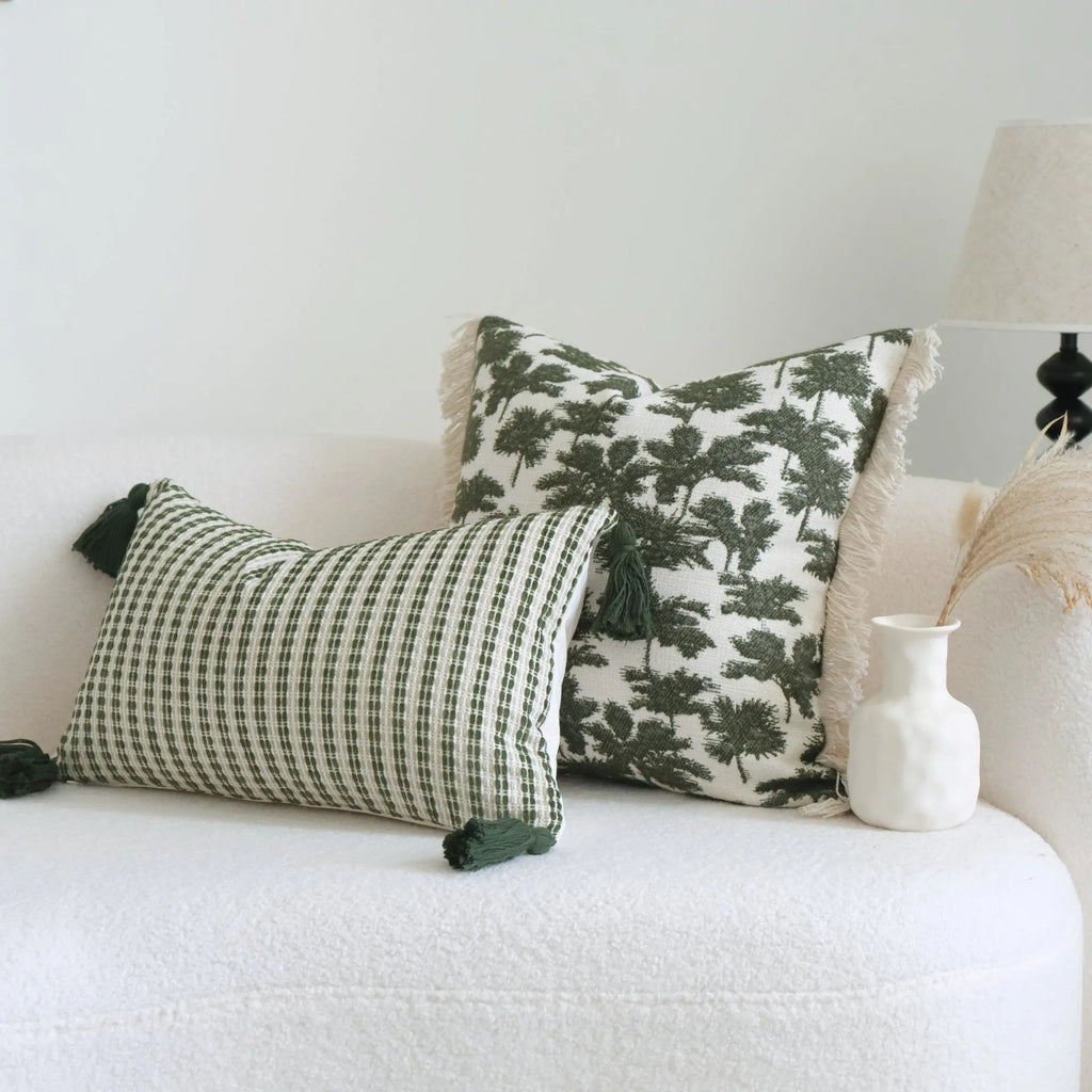 Green striped and leaf patterned hotel pillow with tassel trim on a bed.