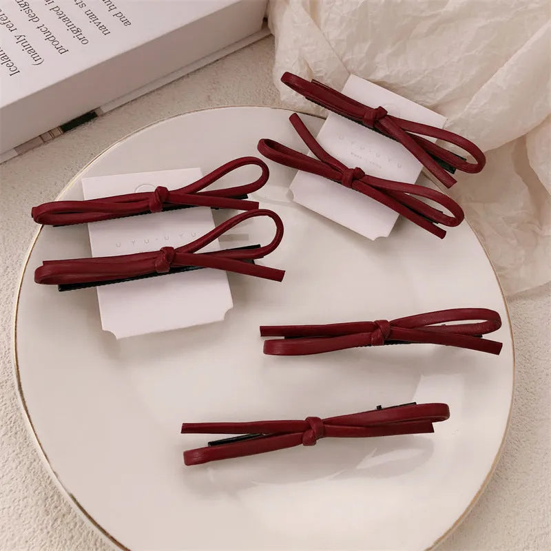 Wine red leather bow barrette hair clip shown on a model or background.
