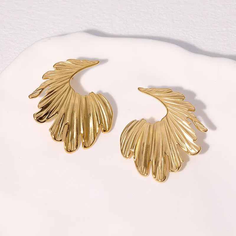 Close-up of a pair of stainless steel leaf-shaped stud earrings on a gold or steel-coloured background.