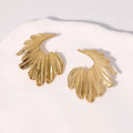 Close-up of a pair of stainless steel leaf-shaped stud earrings on a gold or steel-coloured background.
