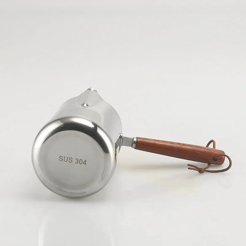 Stainless steel measuring milk cup with wooden handle showing scale markings.