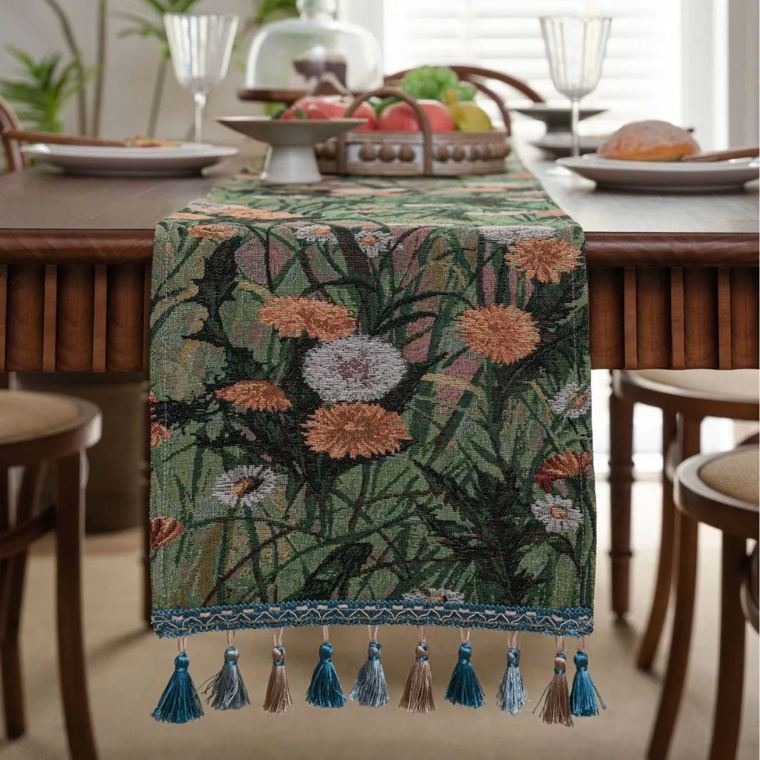 Beige jacquard table runner with floral leaf pattern and long tassels on a dining table.