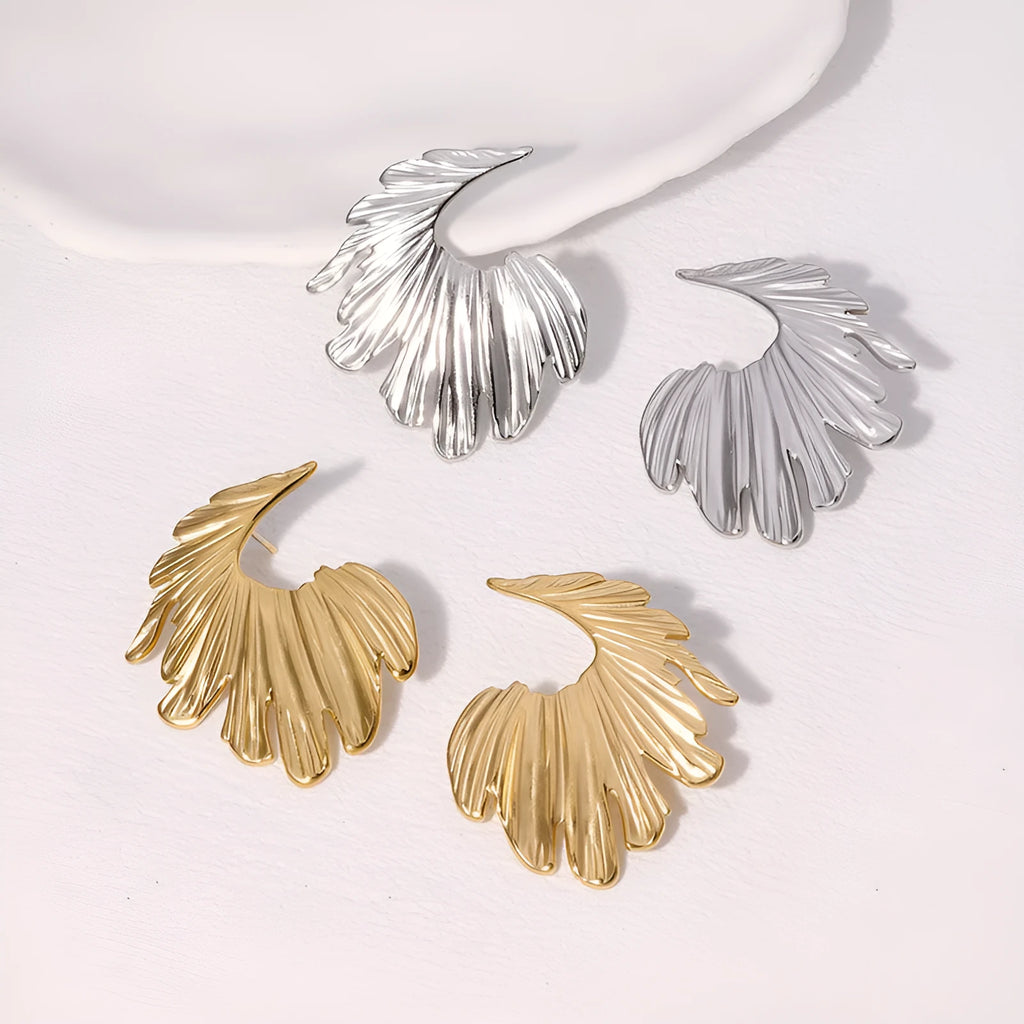 Close-up of a pair of stainless steel leaf-shaped stud earrings on a gold or steel-coloured background.