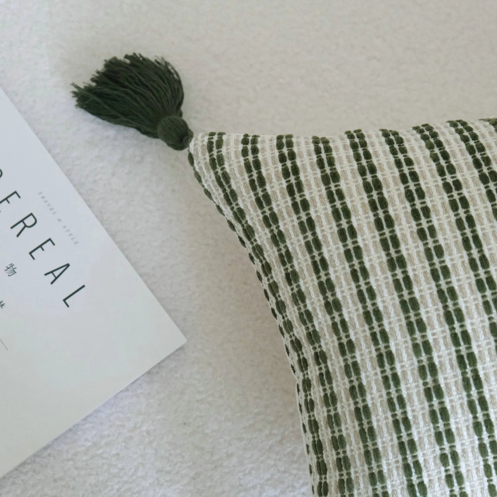 Green striped and leaf patterned hotel pillow with tassel trim on a bed.