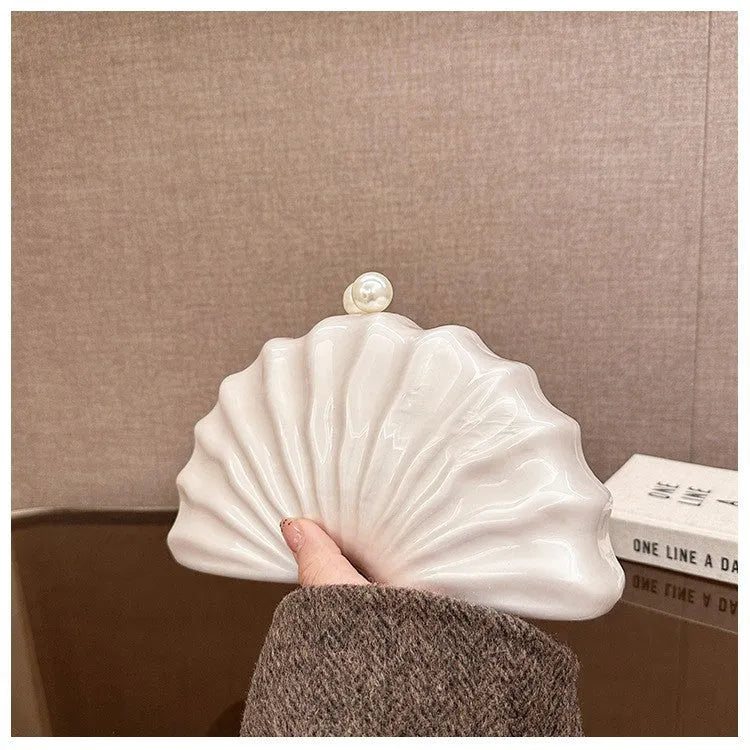 Acrylic shell-shaped clutch bag in champagne colour with chain detail on solid background