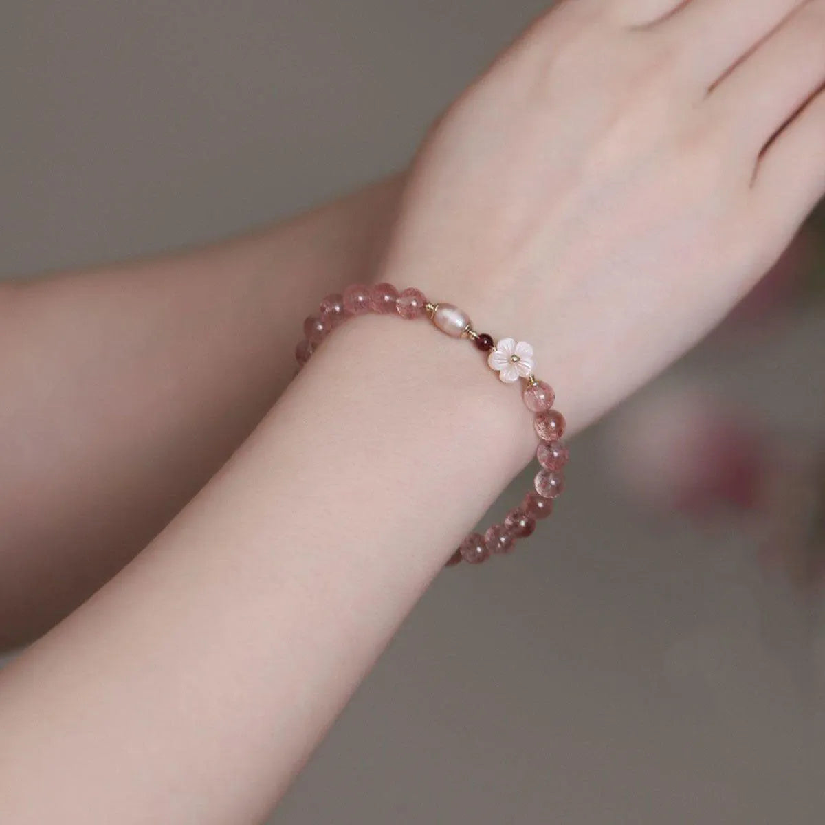 Women's strawberry quartz peach blossom crystal bracelet with floral design on wrist.