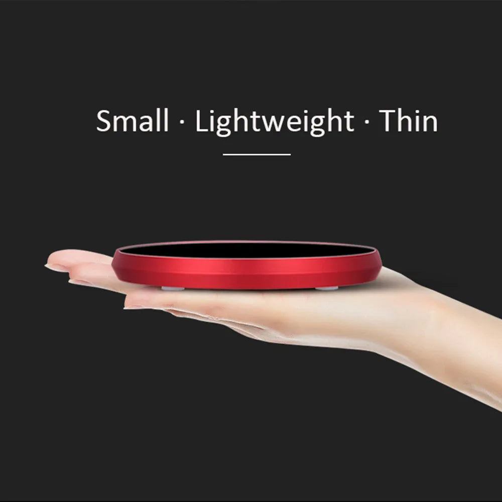 Black USB heating coaster pad for cups with LED indicator light on a wooden desk.