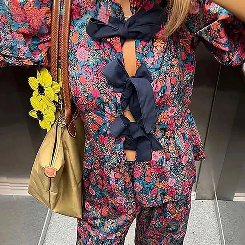 Women's floral print trouser suit set with tie-neck top and puffed sleeves.