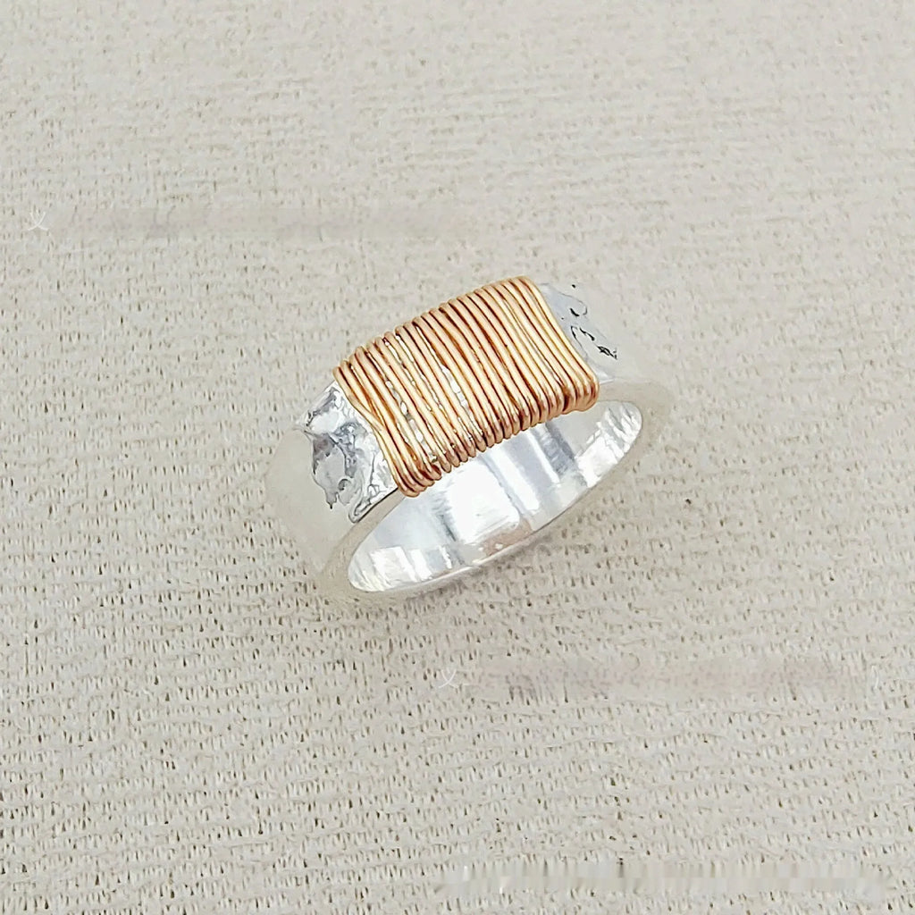 Geometric copper ring bracelet with a wide face and irregular coil design in a silver gold colour.