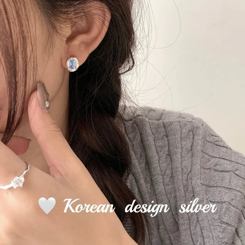 Women's sterling silver earrings with heart-wrapped oval blue diamond centrepiece on silver geometric design
