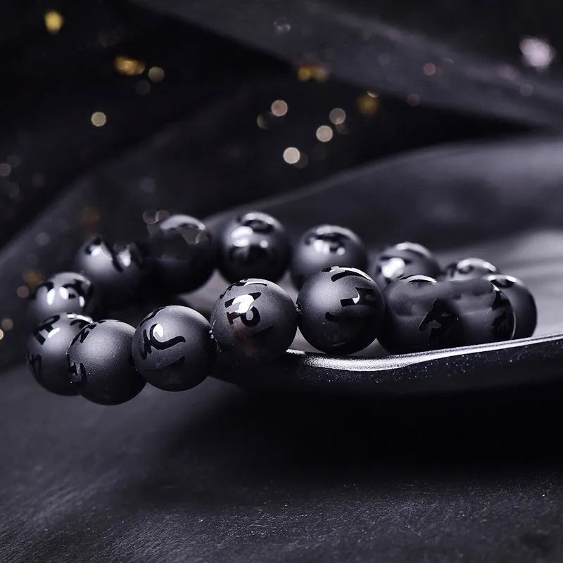 Natural frosted black agate Sanskrit mantra bracelet with Chinese auspicious patterns on a wrist.