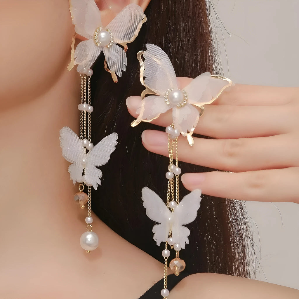 A pair of white butterfly-shaped earrings with tassels, lace details, pearls, and rhinestones.