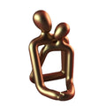 Modern minimalist loving couple resin statue in gold or milky white on a wooden surface.