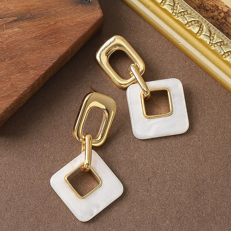 A pair of hollow square geometric earrings with a chamfered edge pattern in a gold tone finish.