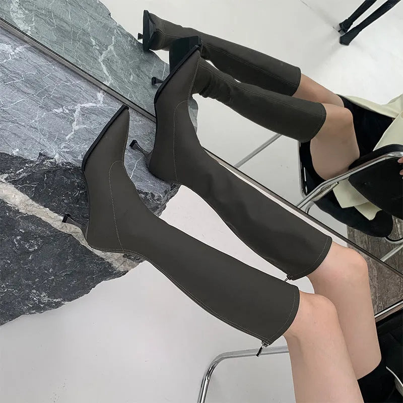 Black women's pointed toe below-the-knee boots with a stiletto heel and back zipper on a plain background.