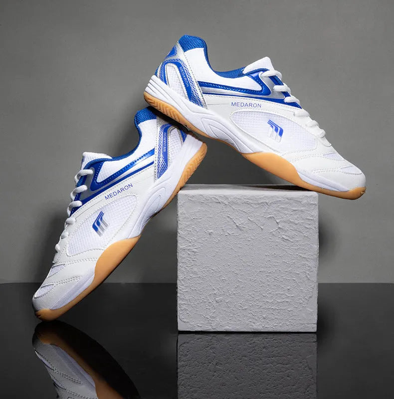 White and blue table tennis shoes with mesh panels and rubber sole on a court surface.