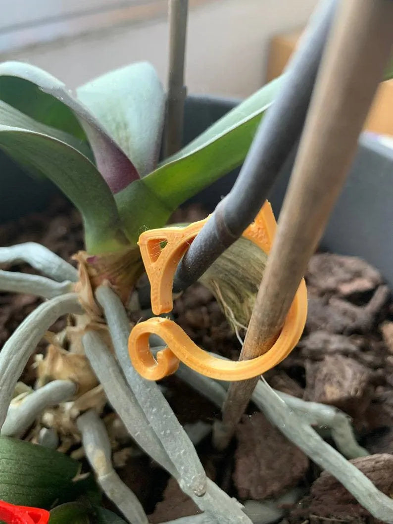 A red plastic cat-shaped plant clip holding a green stem against a garden cane.