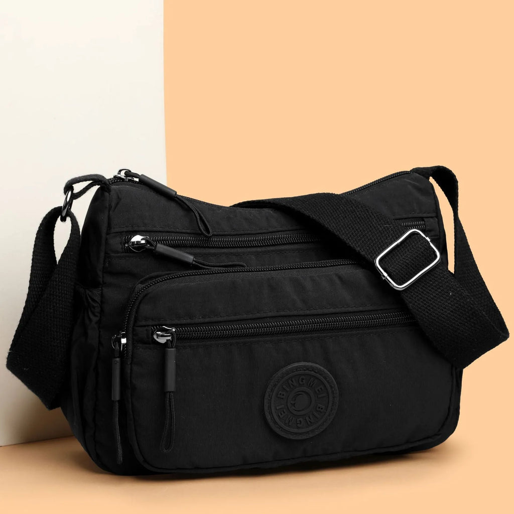 Soft grey nylon crossbody bag with an external pocket and adjustable shoulder strap.