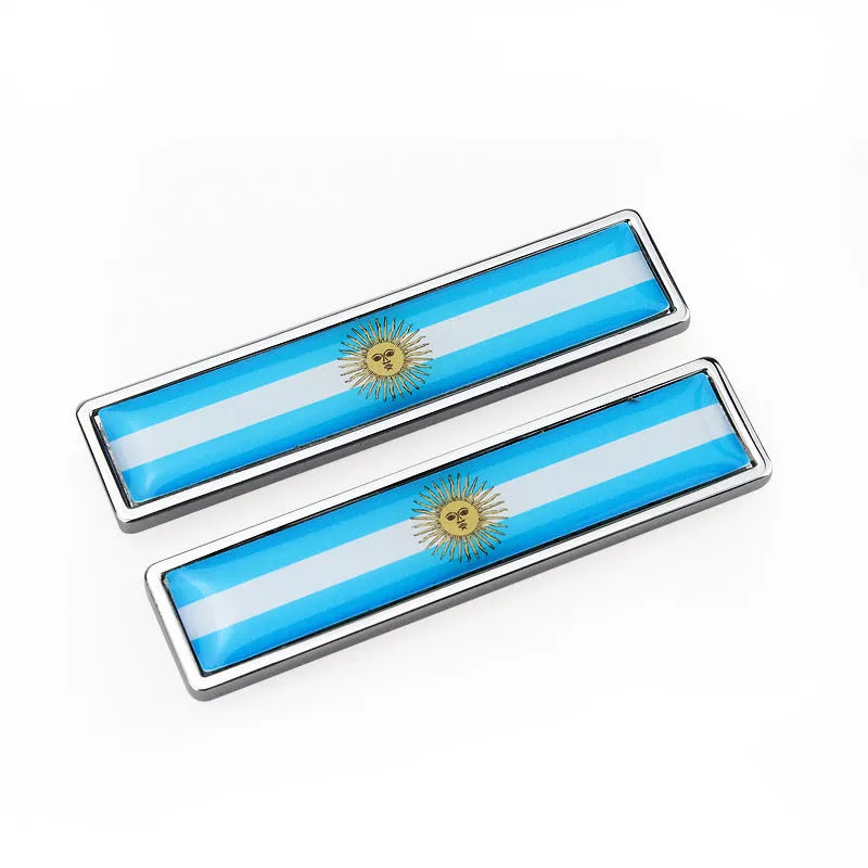 A pair of silver zinc alloy car badge labels with coloured national flag designs, shown at 58mm by 14mm scale.