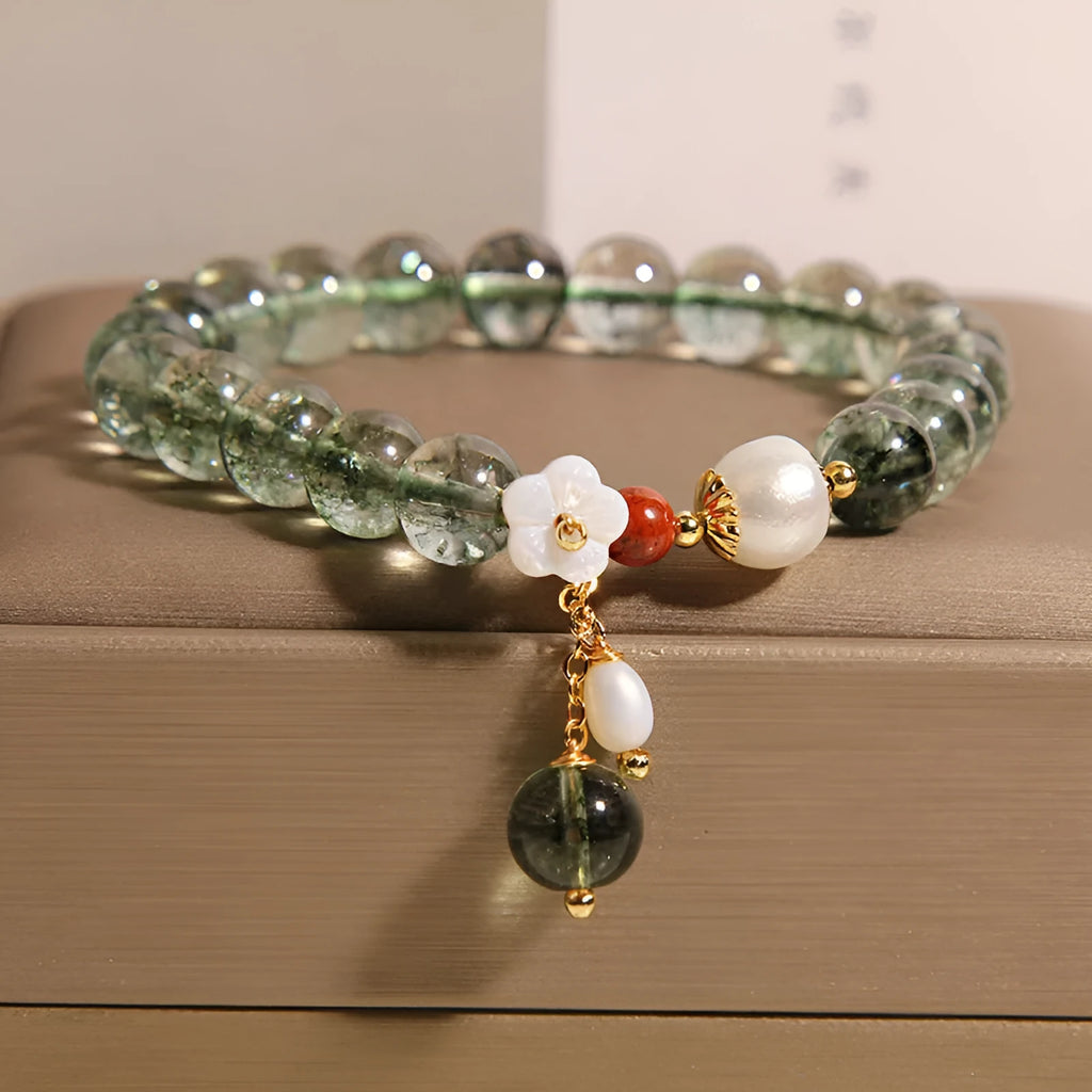 Green phantom quartz crystal bracelet with small shell flower design on woman's wrist.